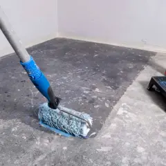 Rodillo aplicando líquido para quitar sintasol del suelo. Bandeja con pintura azul y botella de producto al lado.