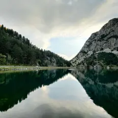 Reflejos perfectos en el ibon de Baños, rodeado de bosques y montañas rocosas. Un paisaje sereno y majestuoso.
