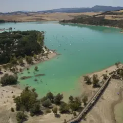 El pantano de Alloz, con sus aguas turquesas, acoge veleros y bañistas. Un puente de madera conecta la orilla con una pequeña isla.