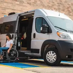 Mujer en silla de ruedas desciende de un minibus vivienda con rampa accesible.