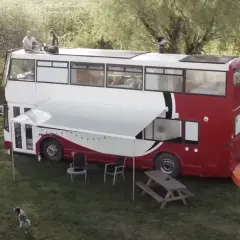 Autobús motorhome de dos pisos con paneles solares en el techo. Personas sentadas en la parte superior, un toldo extendido y muebles de exterior.
