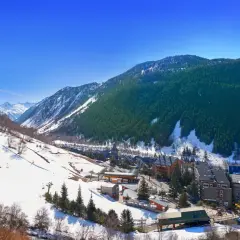 Paisaje nevado del valle de Aran, con pistas de esquí, telesillas y edificios de un pueblo. Ideal para una aventura en autocaravana.