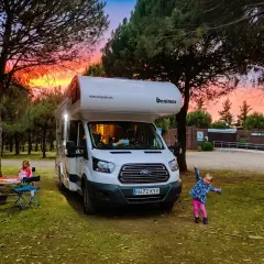 Autocaravana Benimar en un camping al atardecer. Niños jugando y disfrutando.