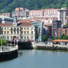 Vista del río Nervión y el Ayuntamiento, un edificio emblemático del bilbao centro storico, con edificios modernos y colinas verdes al fondo.
