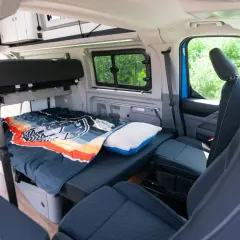 Interior del Ford Nugget con cama lista para dormir, cojín y asientos delanteros.