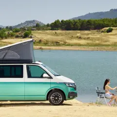 Volkswagen California con baño, lista para una escapada junto al lago. Pareja disfruta de un picnic al aire libre.
