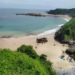 Vista aérea de la playa de Aramal, con arena dorada, aguas turquesas y gente disfrutando del sol y el mar.