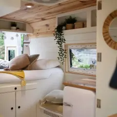 Interior de una camper con cama acogedora, cojines y mantas. Muestra cómo llevar la ropa de forma organizada en este espacio.