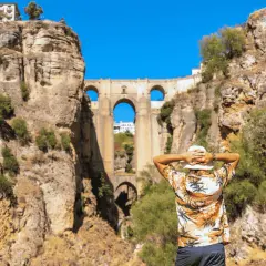 Un hombre con sombrero blanco admira el Puente Nuevo de Ronda en un día soleado.
