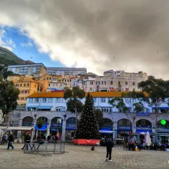 Árbol de Navidad en la plaza de Gibraltar, con edificios coloridos y el Peñón al fondo. Un día nublado, pero festivo.