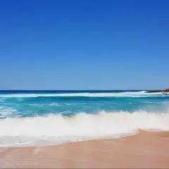 Olas rompiendo en una playa de arena dorada, ideal para saber donde hacer snorkel en Cantabria. Cielo azul intenso.