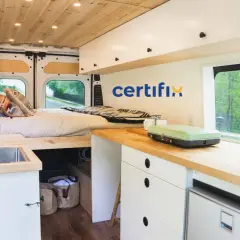 Interior de caravana con cama, fregadero y cocina. Muebles de madera y blancos, ideales para fabricantes de muebles para caravanas.