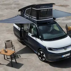 La vw california electrica lista para la aventura, con toldo extendido, mesa y sillas, lista para disfrutar del aire libre.