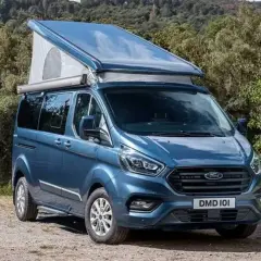 Furgoneta camper azul Westfalia Nugget con techo elevable, lista para una aventura en la naturaleza.