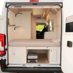 Interior de una camper con cama, almacenamiento y un pequeño equipaje. La altura camper permite aprovechar cada rincón.