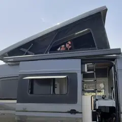 Mujer asomada en la cama elevada de una furgoneta camper. Las medidas de esta furgoneta man son perfectas para viajar.