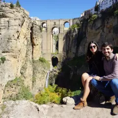 Pareja sonriente posa frente al impresionante Tajo de Ronda, con el Puente Nuevo y la cascada de fondo. Un recuerdo imborrable de la ronda altstadt.