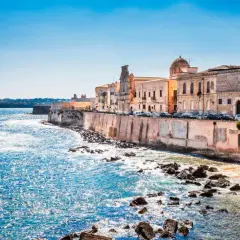 Costa de Siracusa, Sicilia, con edificios históricos y el mar azul brillante.