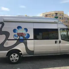 Furgoneta camperizada con motor Ford 2.2 TDCI 140 CV. Decoración de flor azul y carretera gris.
