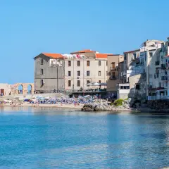 Edificios antiguos y una animada cefalu playa con gente disfrutando del sol y el mar azul.