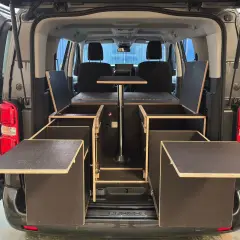 Soluciones de trucos almacenaje furgonetas camper: módulos de madera con compartimentos y mesa abatible para maximizar el espacio.