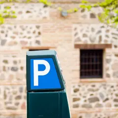 Parquímetro azul con letra P blanca, señalando opciones de altstadt Marbella parken. Edificio de piedra y ladrillo al fondo.