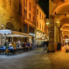 Noche en Bolonia, con gente cenando bajo toldos. Imagina cómo ir de Milán a Bolonia y disfrutar de esta escena.