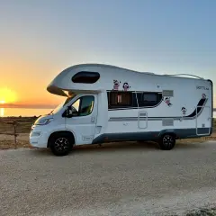 Autocaravana blanca aparcada junto al mar al atardecer. ¡La aventura de **Sicilia en autocaravana** comienza!