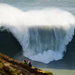 Dos personas observan desde un mirador las gigantescas olas de Nazaré, un espectáculo natural impresionante.