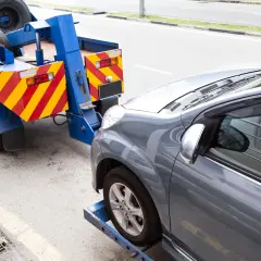 Grúa azul lista para transportar caravana. El coche gris está asegurado en la plataforma.