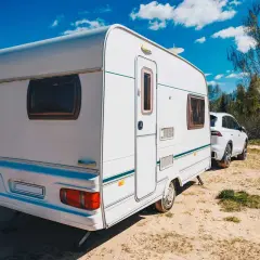 Caravana blanca lista para el transporte, aparcada junto a un coche en un día soleado.