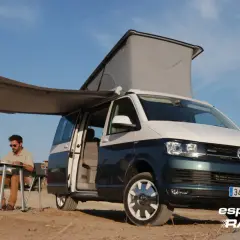 Hombre sentado en mesa plegable bajo toldo de camper en playa, con medidas california beach.
