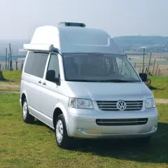 Furgoneta Volkswagen Transporter T5 camperizada con techo elevable, aparcada en un prado con vistas a un valle.