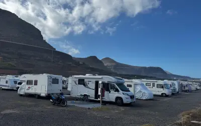 Un grupo de autocaravanas low cost aparcadas en un terreno pedregoso, con montañas y cielo azul de fondo.