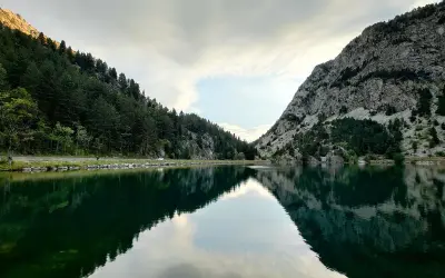 Reflejos perfectos en el ibon de Baños, rodeado de bosques y montañas rocosas. Un paisaje sereno y majestuoso.