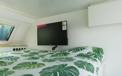 Cama con sábanas de hojas verdes y un televisor de consumo tv 50 pulgadas colgado en la pared.
