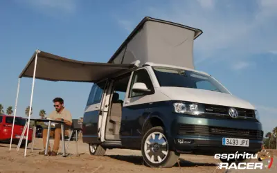 Hombre sentado en mesa plegable bajo toldo de camper en playa, con medidas california beach.