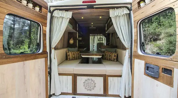 Interior de una caravana camperizada con asientos, mesa y decoración rústica. ¡Perfecta para aventuras!