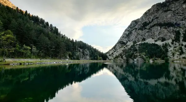Reflejos perfectos en el ibon de Baños, rodeado de bosques y montañas rocosas. Un paisaje sereno y majestuoso.