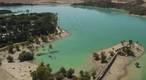 El pantano de Alloz, con sus aguas turquesas, acoge veleros y bañistas. Un puente de madera conecta la orilla con una pequeña isla.