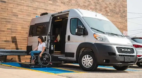 Mujer en silla de ruedas desciende de un minibus vivienda con rampa accesible.