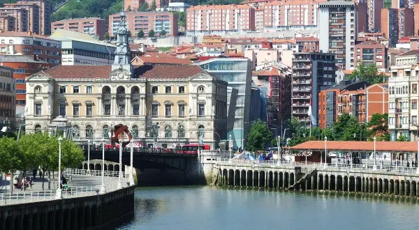 Vista del río Nervión y el Ayuntamiento, un edificio emblemático del bilbao centro storico, con edificios modernos y colinas verdes al fondo.
