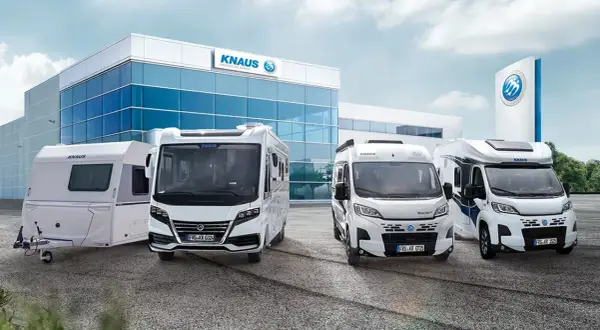Una caravana y tres autocaravanas KNAUS blancas frente a un edificio moderno.