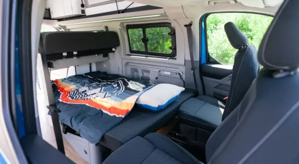 Interior del Ford Nugget con cama lista para dormir, cojín y asientos delanteros.