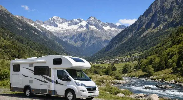 Autocaravana aparcada junto a un río en un valle alpino con picos nevados, ideal para explorar los ibones de Benasque.