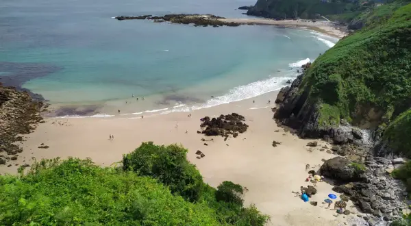 Vista aérea de la playa de Aramal, con arena dorada, aguas turquesas y gente disfrutando del sol y el mar.