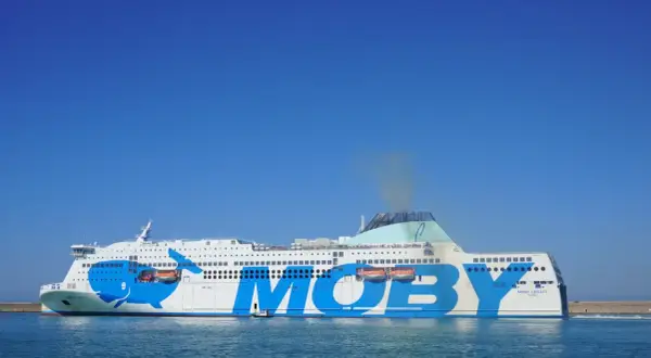 El ferry Moby Legacy, con su icónico diseño de ballena azul, navega rumbo a Cerdeña o Sicilia bajo un cielo despejado.