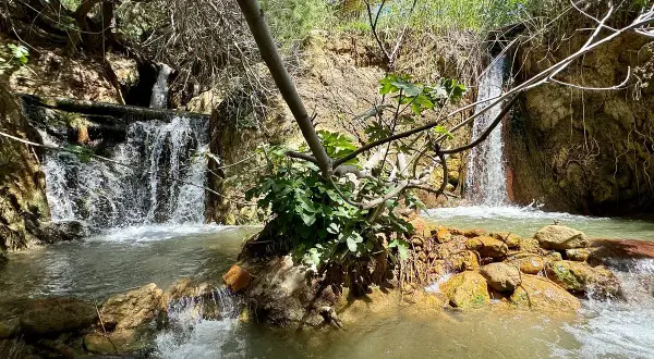 Cascada natural en las aguas termales Santa Fe, con rocas anaranjadas y vegetación exuberante.