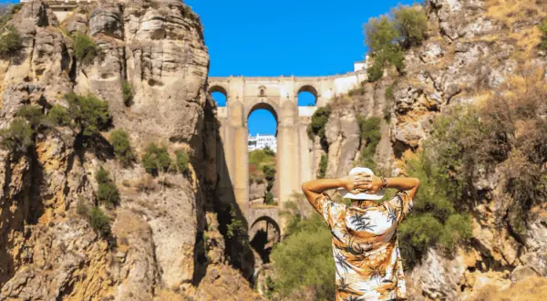 Un hombre con sombrero blanco admira el Puente Nuevo de Ronda en un día soleado.