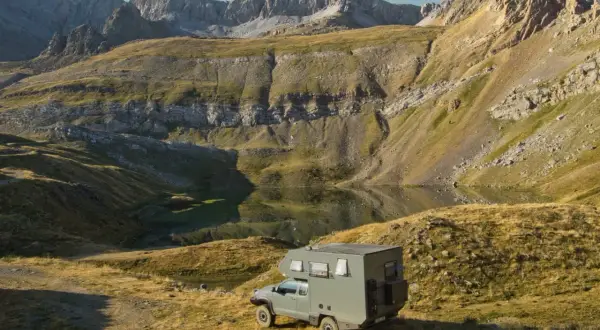 Una camper lista para la aventura en la Transpirenaica, aparcada junto a un lago de montaña con imponentes picos rocosos al fondo.